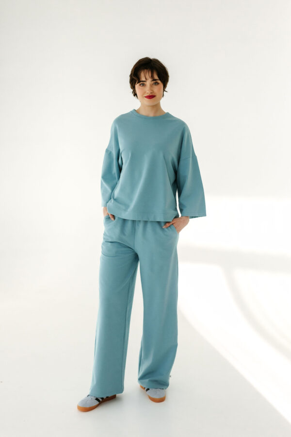 Kobieta w komplecie dresowym baby blue, stojąca w promieniach słońca, prezentująca modny oversize’owy look.